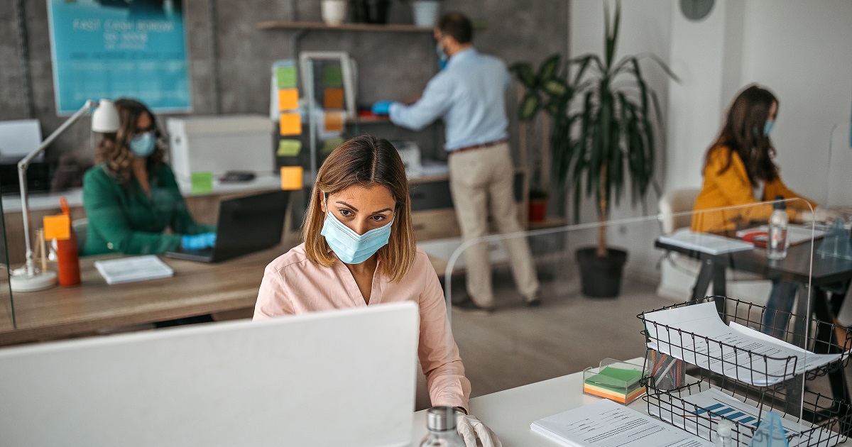 Professionals work in an office wearing masks and social distancing