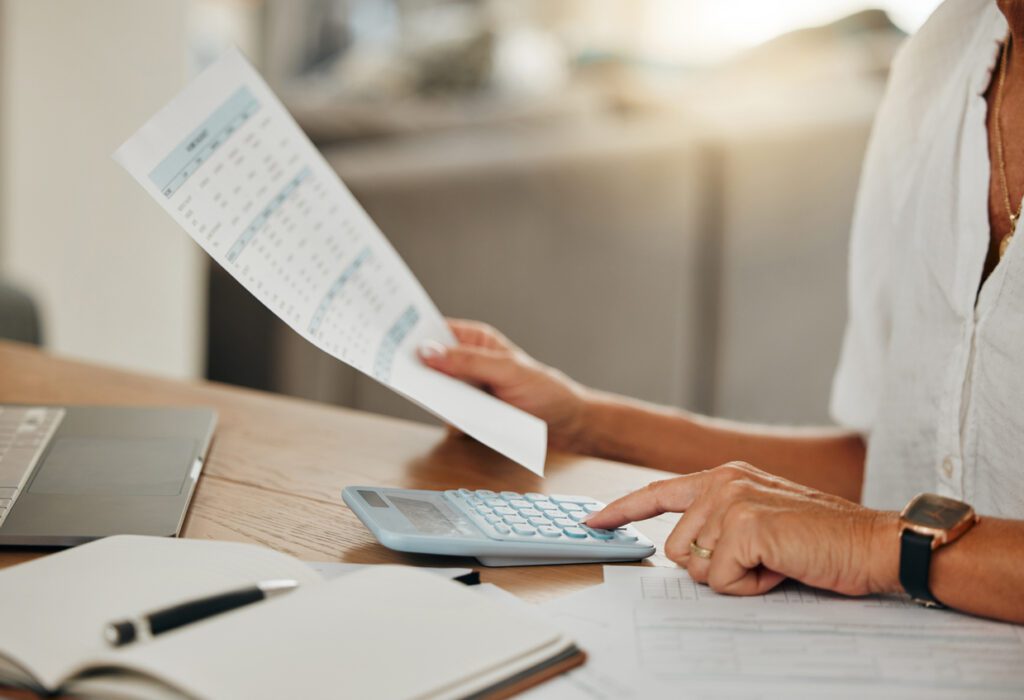 Hands, small business finance and calculator for budget, expenses or paper bills at home. Hand of accountant or employee calculating financial income of investments in planning and scheduling work