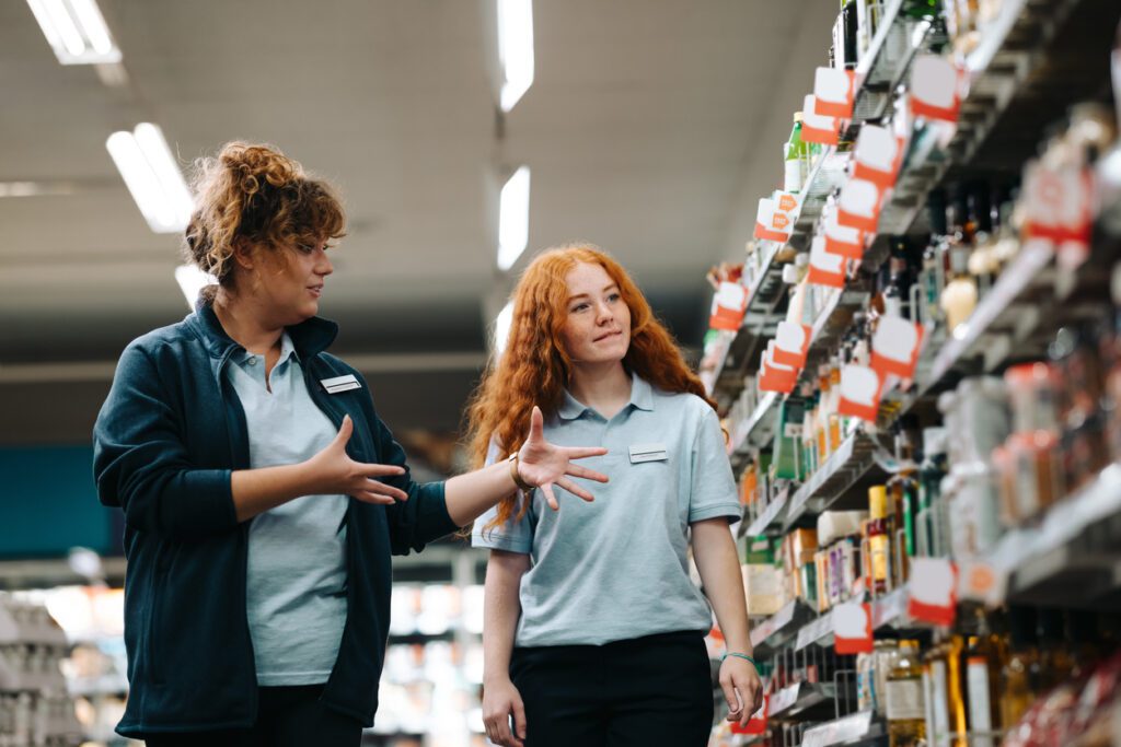 Grocery store manager training new female worker with red hair