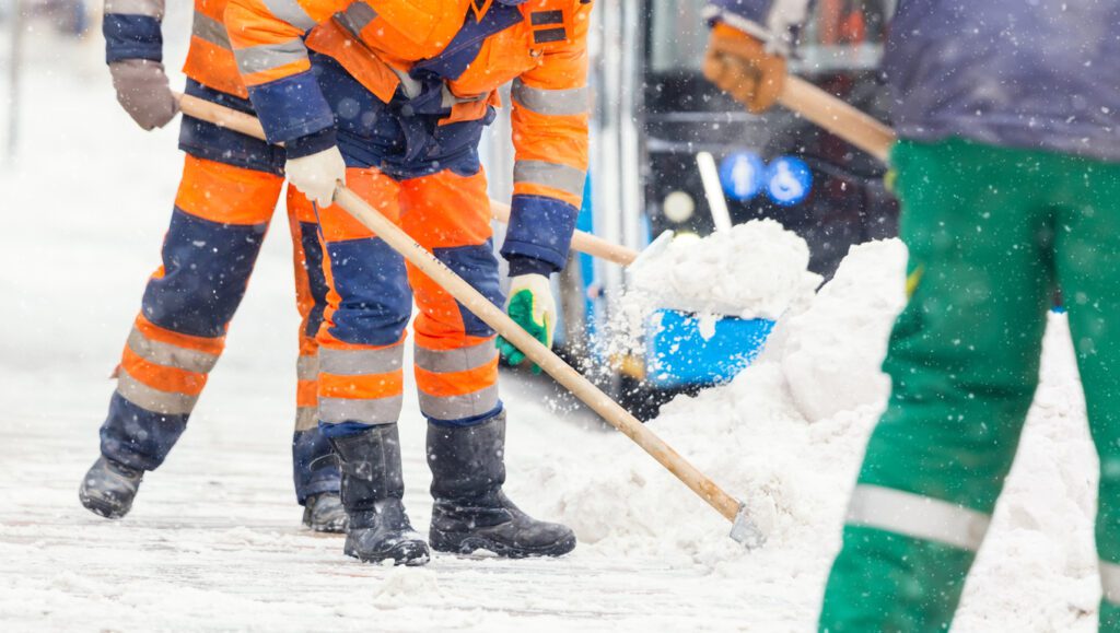 Communal services workers sweep snow from road in winter. 
