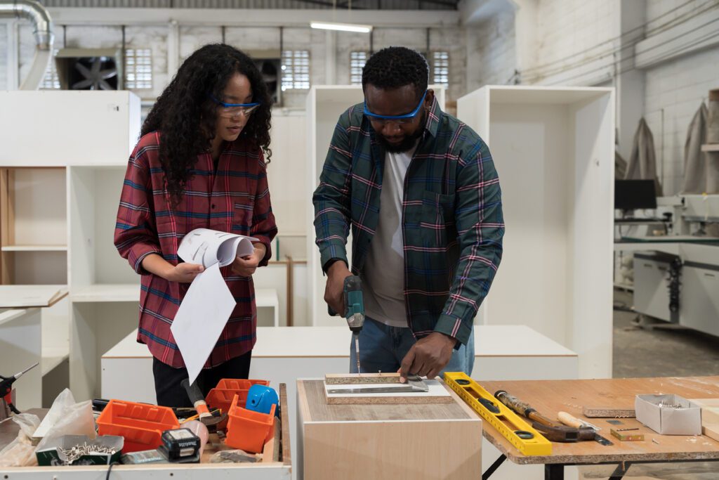 Two worker working together, using carpenter tools in furniture factory