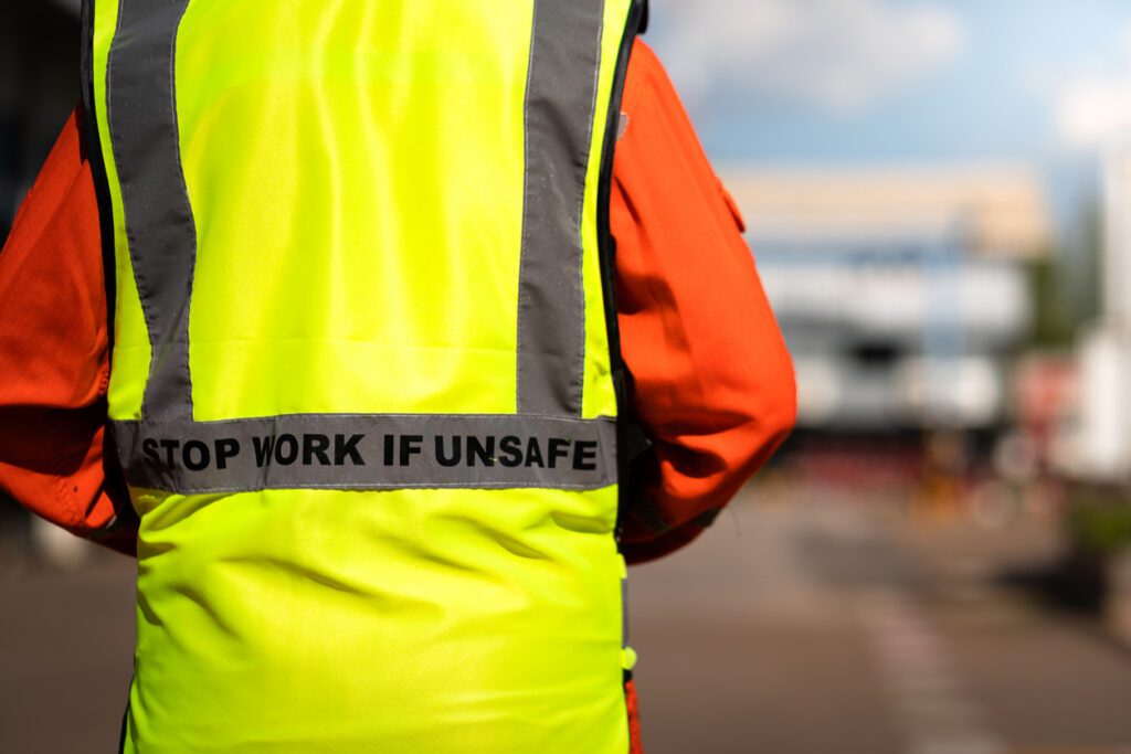 Close-up at "Stop work if unsafe" sign label on back of reflective vest which is wear by a lifting signaler worker. Safety conception photo for heavy industry operation.