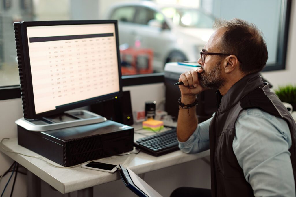 Foreman of auto mechanic workshop using desktop PC in the office.