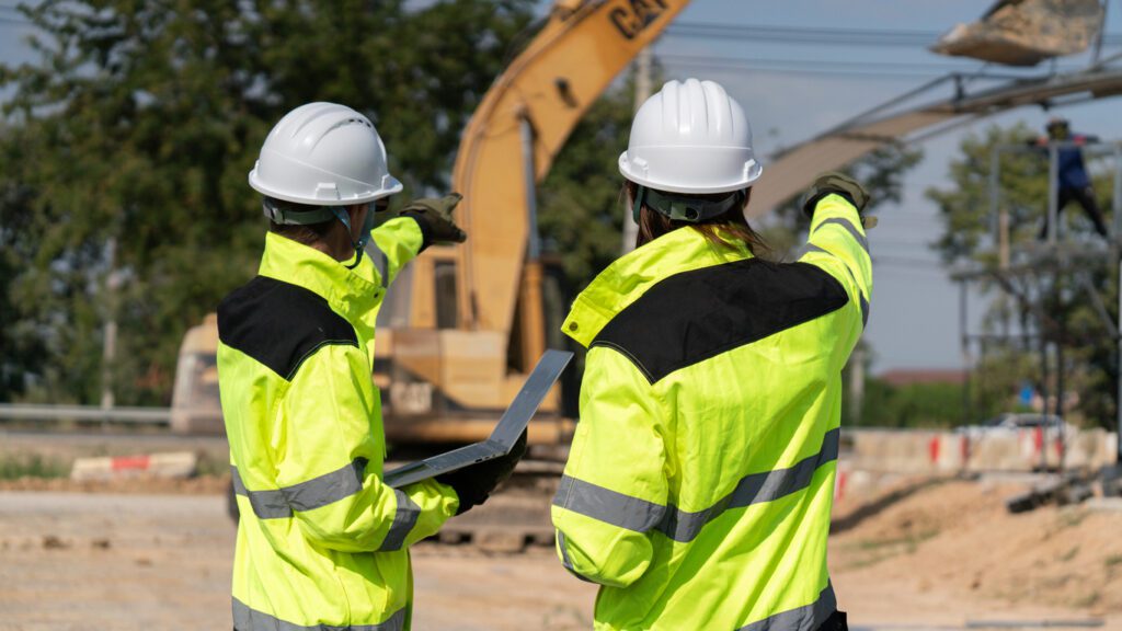 A civil engineer, architect, or construction worker is wearing a safety suit while inspecting building construction on site and verifying blueprints or drawing plans.