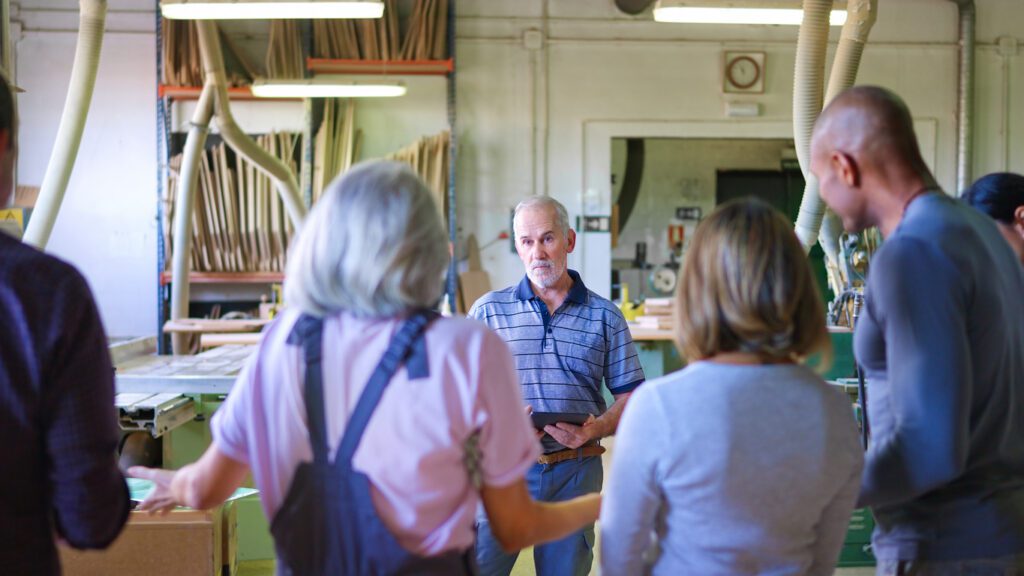 Senior instructor giving carpentry direction to group of blue-collar employees, sharing expertise