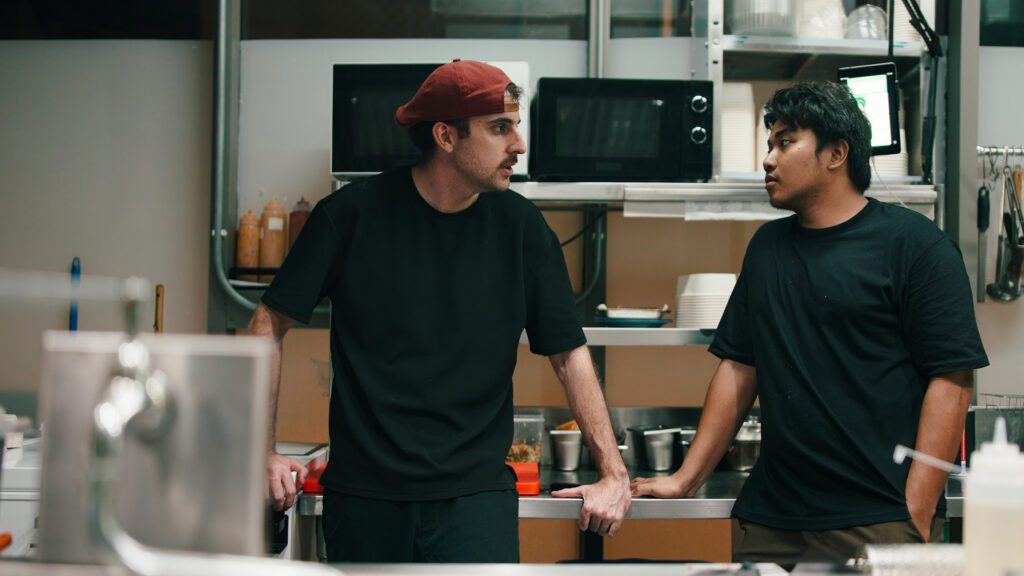Kitchen staff standing at counter in busy dark restaurant or ghost kitchen environment, brainstorming