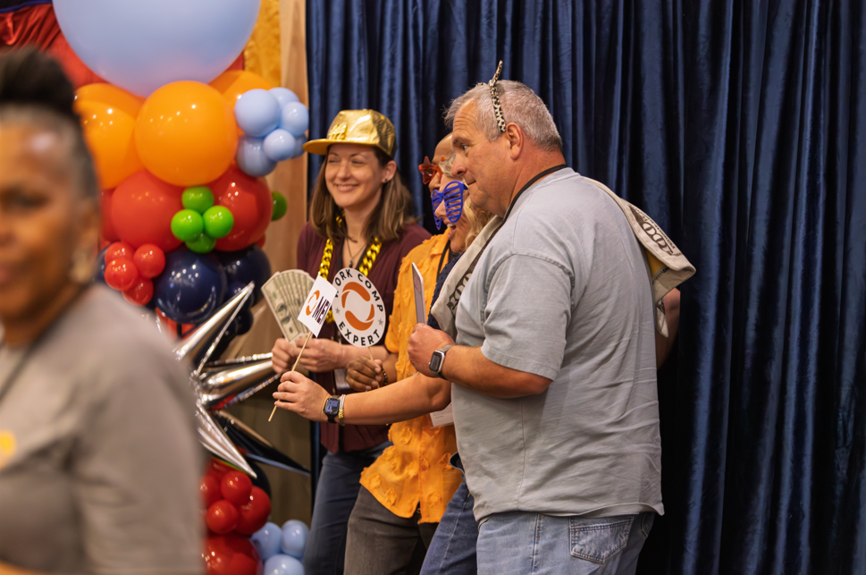 Three people celebrating at a company event with balloons in the background.