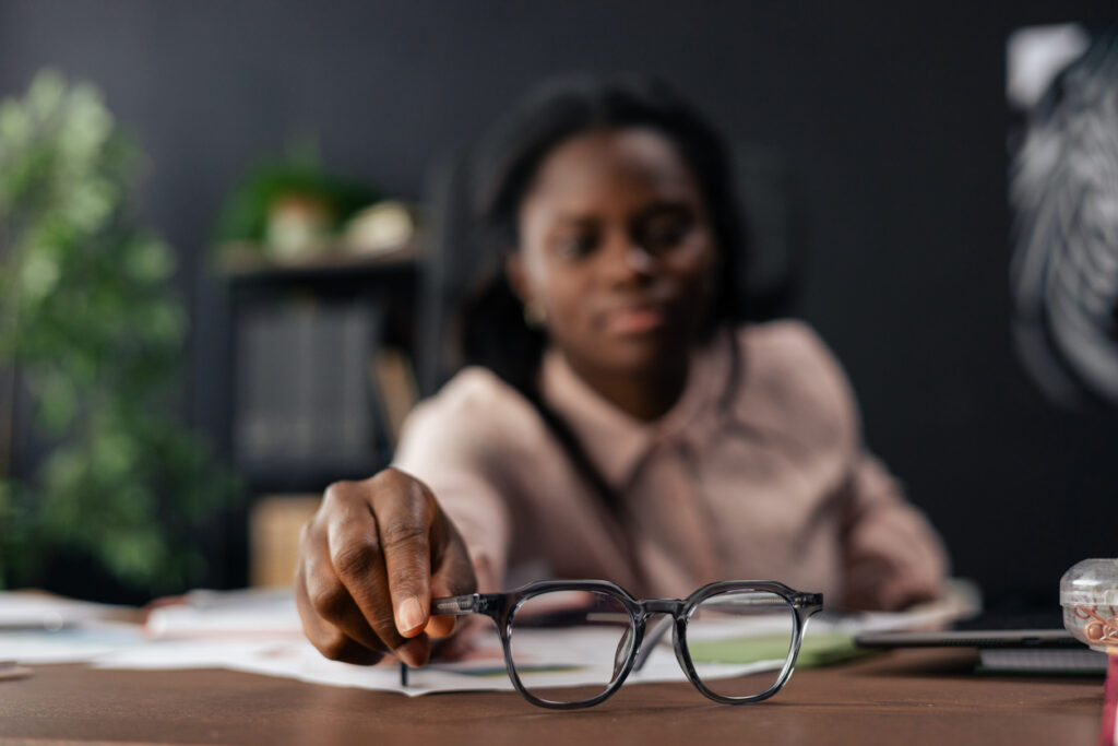 Woman reaching out to pick up her reading glasses during work in an office